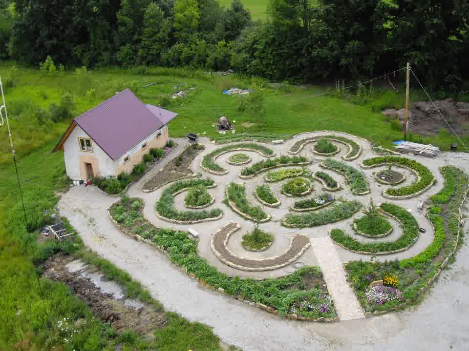 A circular garden labyrinth beside a small house, seen from above