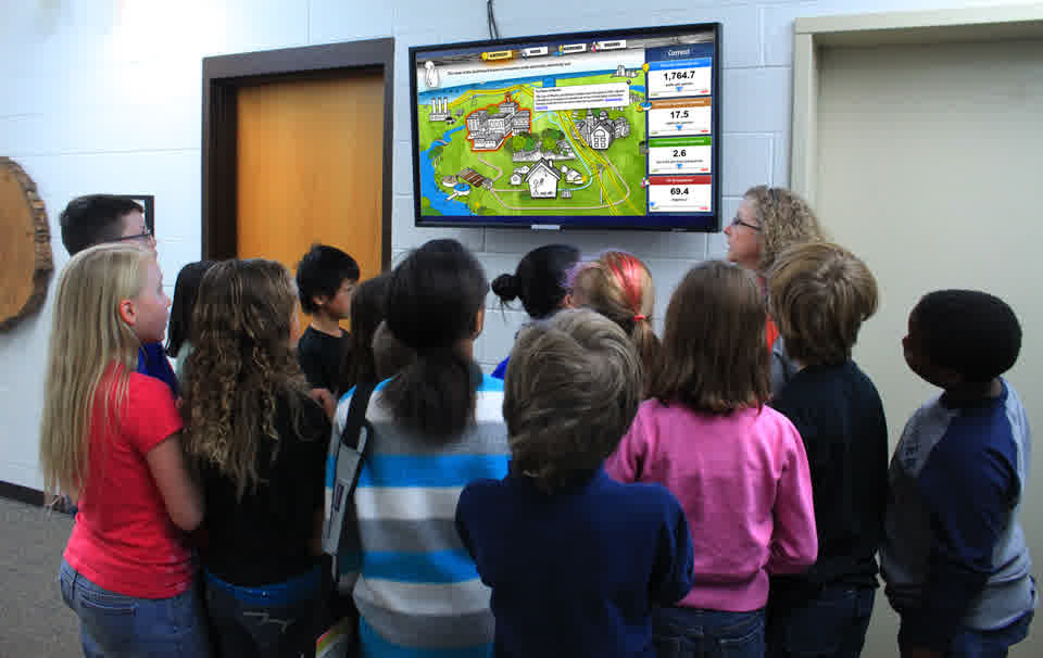 Children and a teacher gathered around a dashboard screen in a school hallway