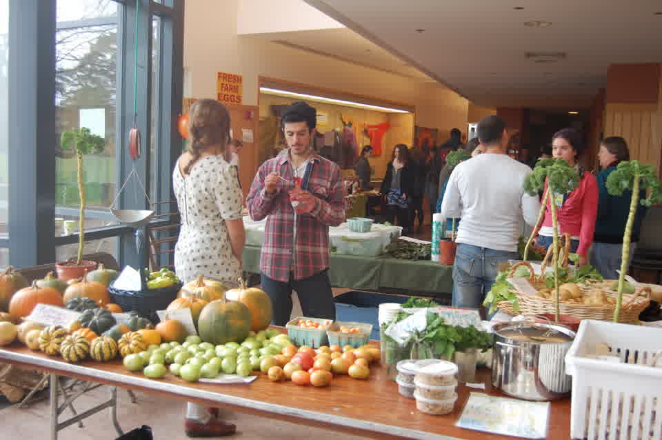 Shoppers and vendors at an indoor market with vegetables and pumpkins