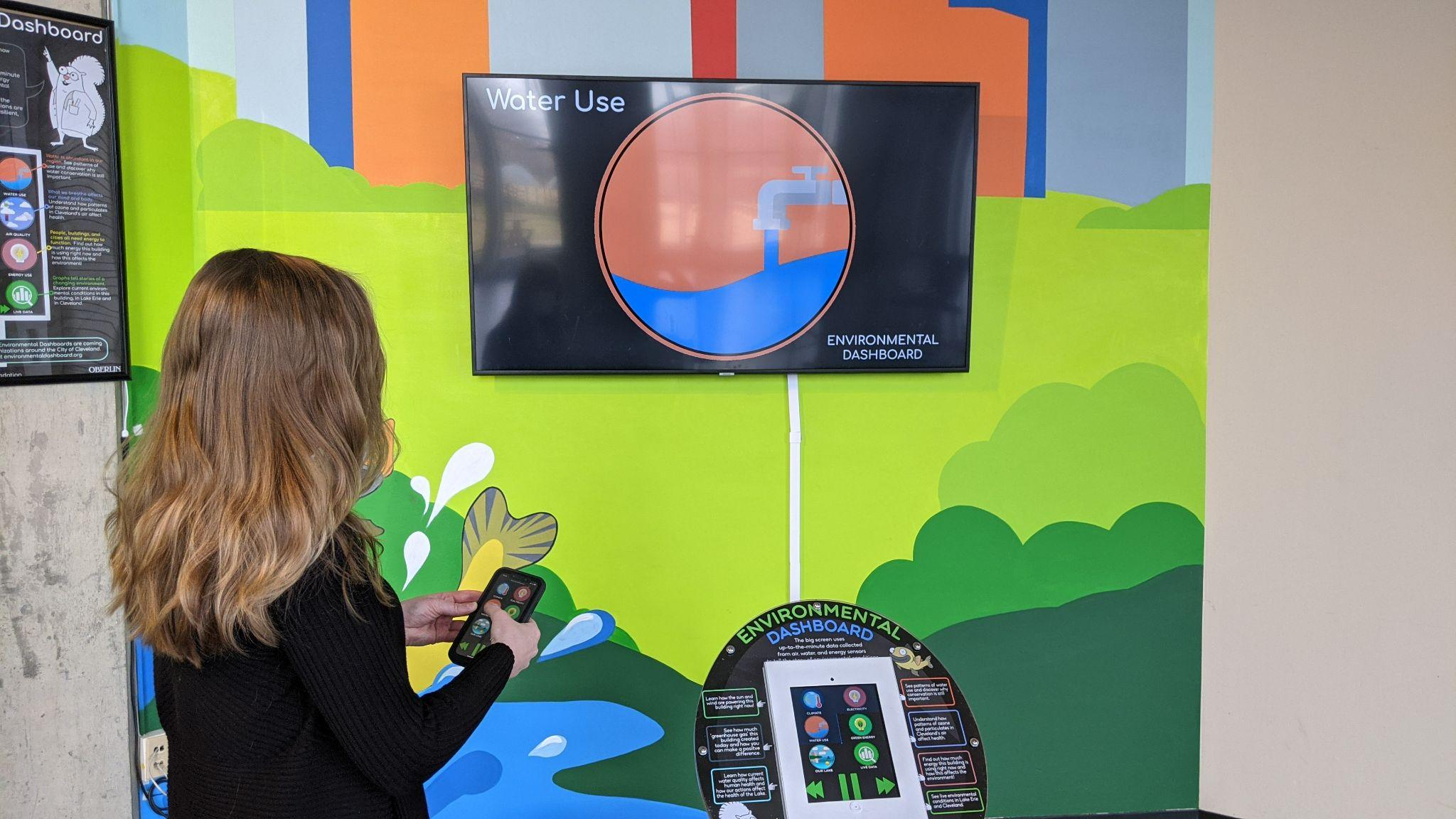 A visitor holds the phone controller beside a large display showing Water Use