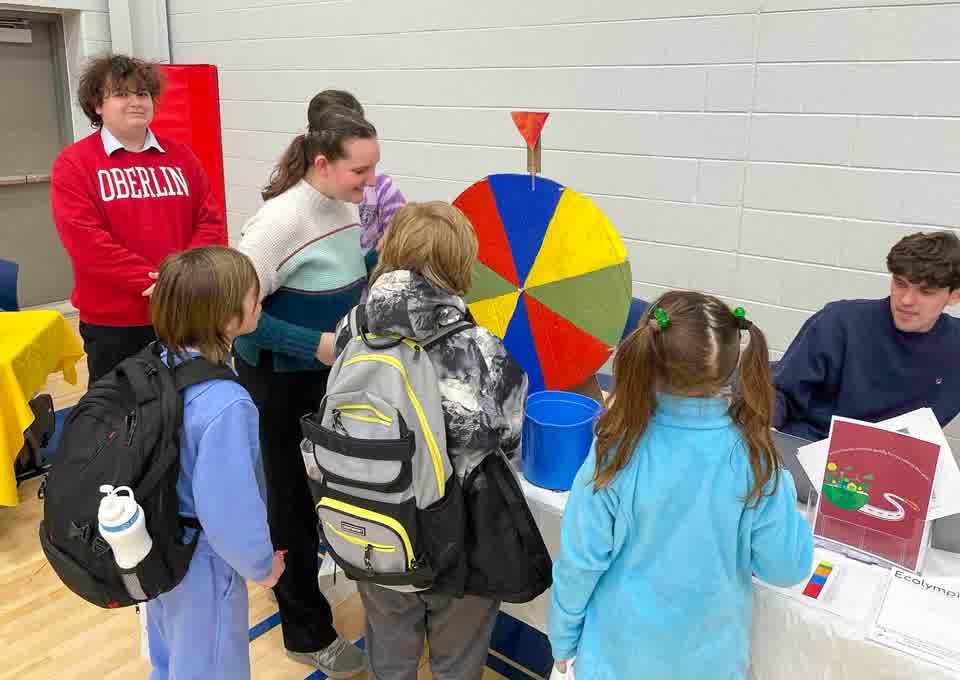 College students in Oberlin sweatshirts run an activity table with a prize wheel for local children